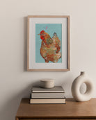 Framed artwork of a hen on a wall above books and a vase.